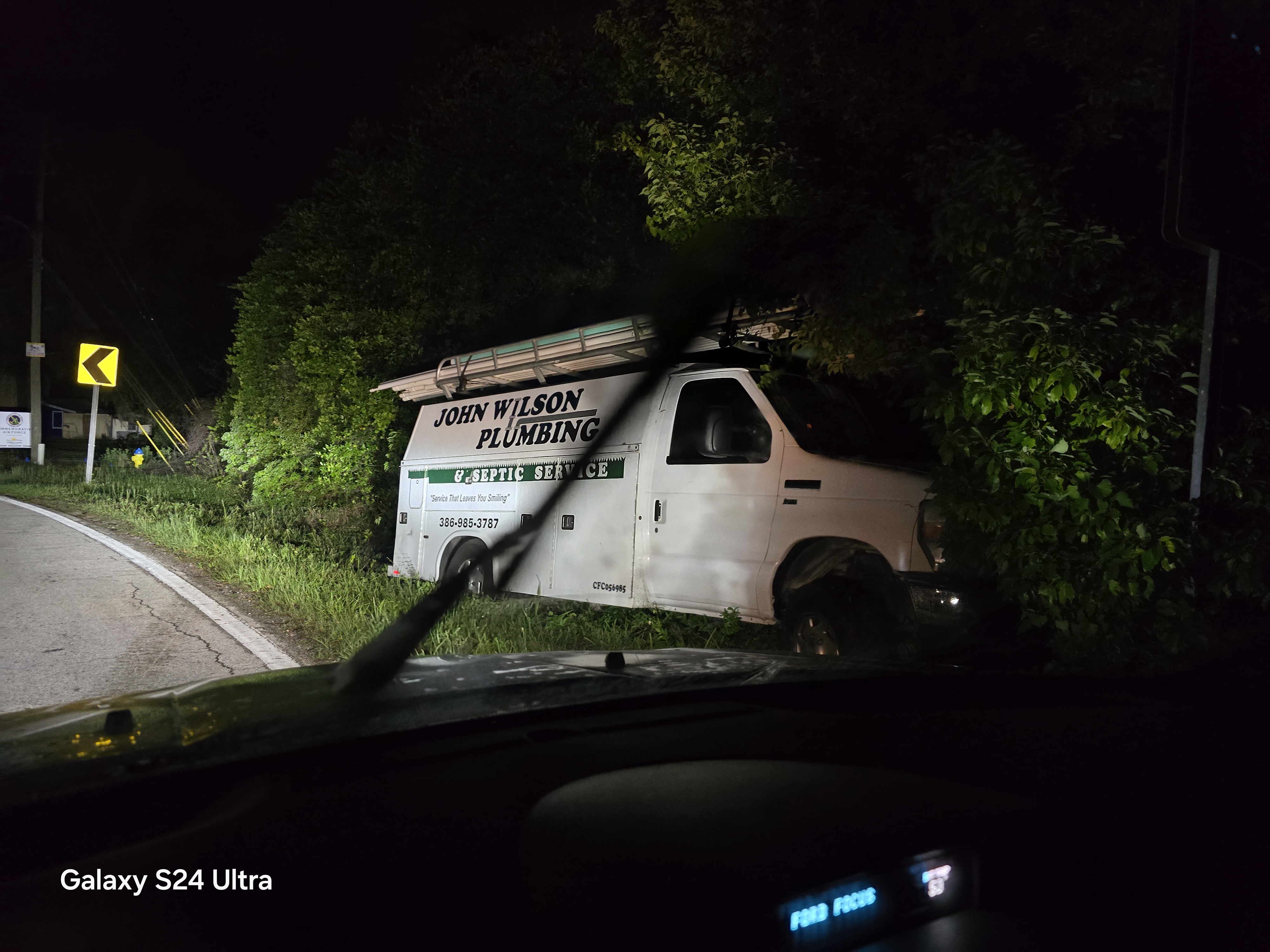 Service truck in brush at curve with yellow Turn-ahead warning sign visible