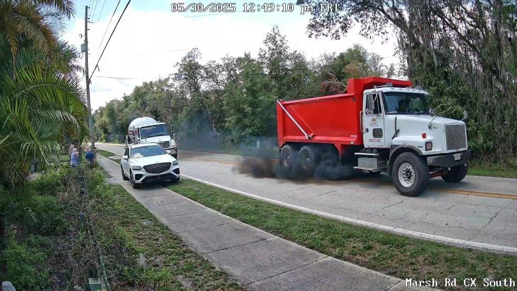 Red dump truck forcing white SUV to edge of road